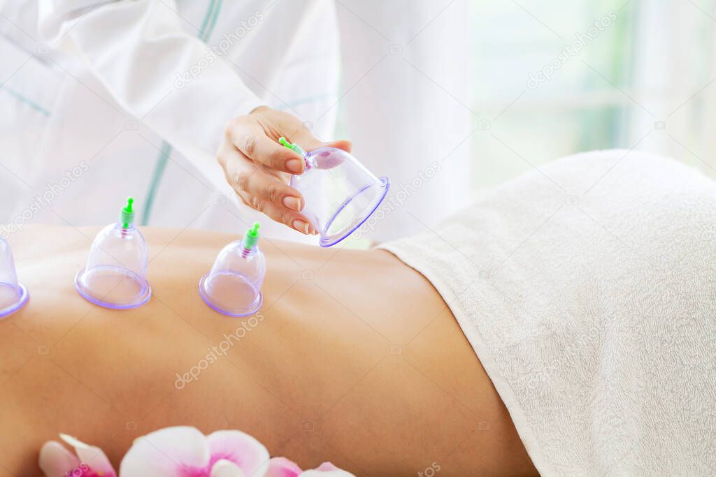 Woman getting anti-cellulite massage of back with use of vacuum cans