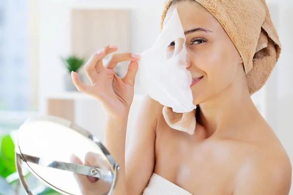 Mulher aplica pano branco máscara hidratante em seu rosto — Fotografia de Stock