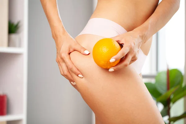 Cellulit problem koncepcja, młoda kobieta trzyma pomarańczowy w pobliżu nogi — Zdjęcie stockowe