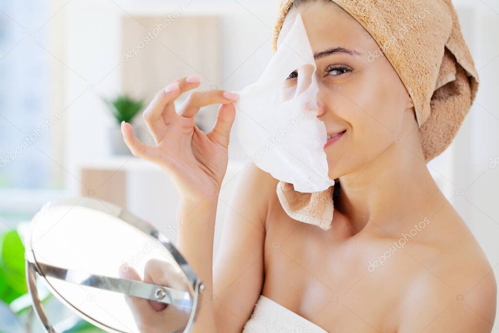 Woman applies white cloth moisturizing mask on her face