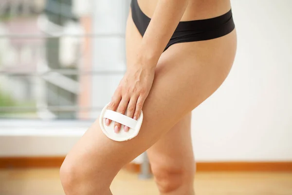 Cellulite treatment, woman arm holding dry brush to her leg. — Fotografia de Stock