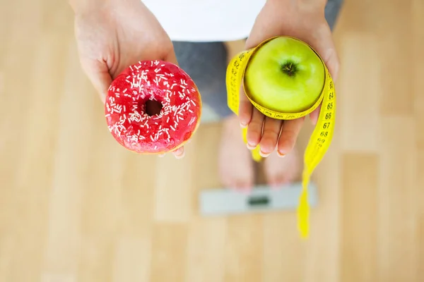Vrouwen kiezen tussen donut en groene appel tijdens haar dieetsessie. — Stockfoto