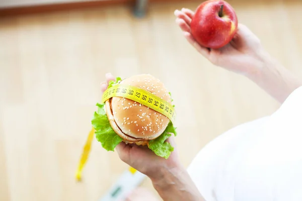 Dieta concetto, donna in possesso di una scelta di hamburger dannosi e mela fresca. — Foto Stock