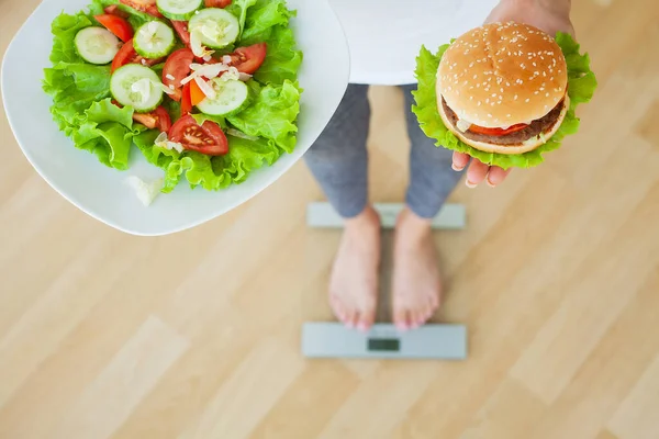 Dieta concetto, donna che sceglie tra hamburger spazzatura e insalata fresca — Foto Stock