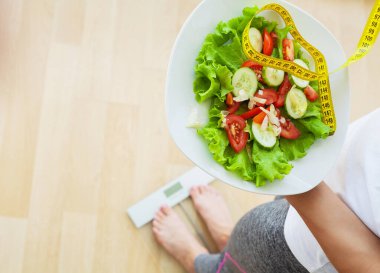 Woman measures weight on electronic scales and diet salad