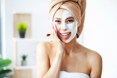Beautiful young woman is getting facial clay mask at spa