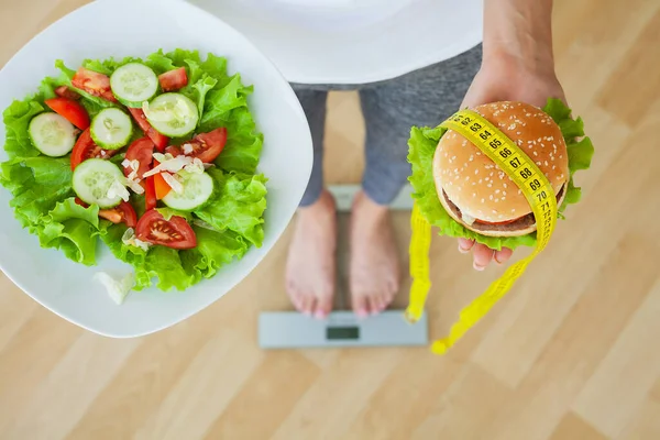 Dietní koncept, žena vybírá mezi nezdravým hamburgerem a čerstvým salátem — Stock fotografie