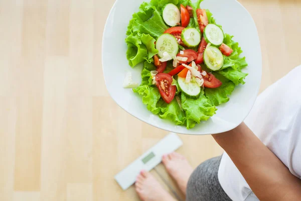 Жінка вимірює вагу на електронних вагах та дієтичному салаті — стокове фото