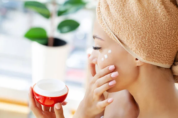 Mulher bonita aplicando creme hidratante em seu rosto — Fotografia de Stock