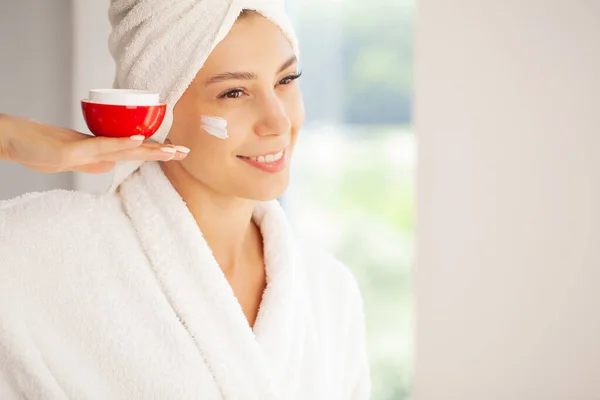 Smiling young woman applies cream on her face — Foto de Stock