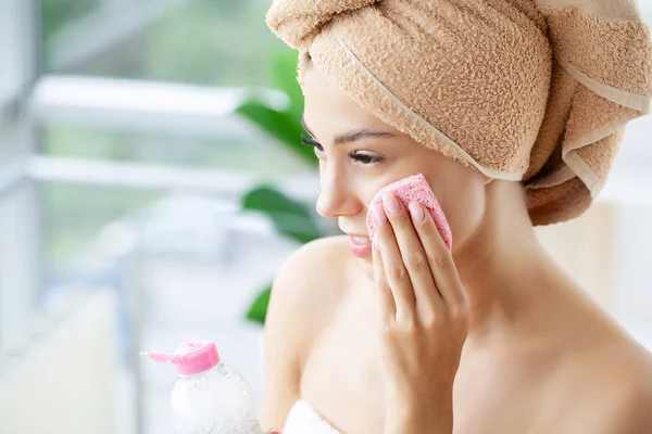 Улыбающаяся женщина с завернутой в голову полотенце губкой для лица — стоковое фото