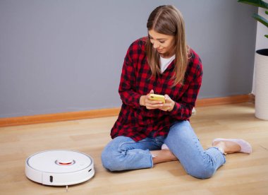 Robot elektrik süpürgesi evde çalışırken dinlenen bir kadın.