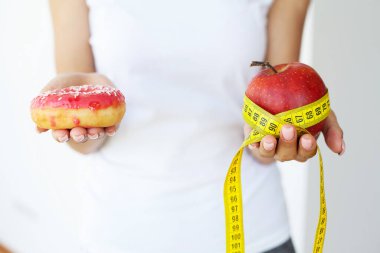 Zararlı çörek ve taze elma seçeneğini elinde tutan kadın..