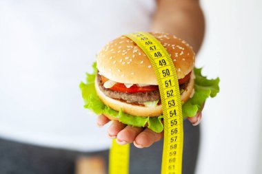 Zararlı bir hamburgerle sarı mezura tutan bir kadın.