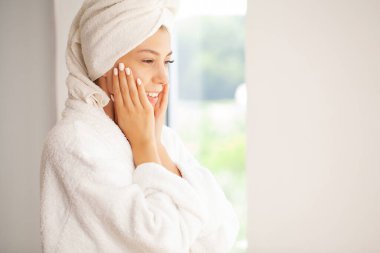 Neşeli genç bir kadın yüzüne nemlendirici krem sürüyor.