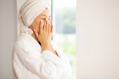 Gülümseyen genç kadın nemli yüz kremi sürüyor..