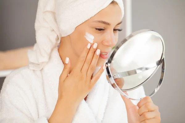 Fröhliche junge Frau trägt Feuchtigkeitscreme auf das Gesicht auf — Stockfoto