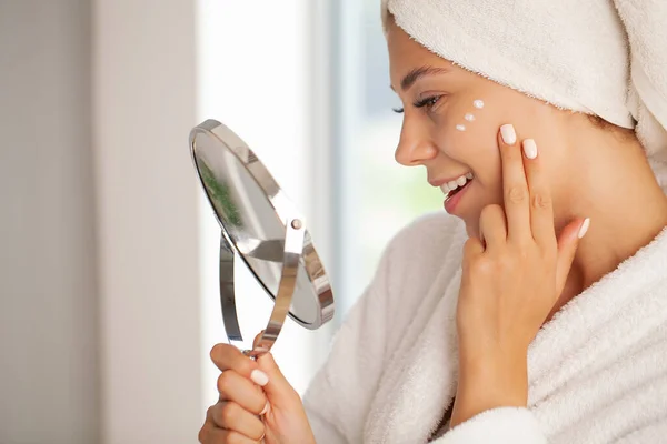 Hermosa modelo aplicando tratamiento de crema cosmética en su cara — Foto de Stock