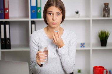 Mutsuz kadın hap ve bir bardak su tutuyor.