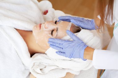 Kozmetik uzmanı spa salonundaki kadına çarşaf maskesi takıyor.