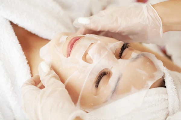 Kozmetik uzmanı spa salonundaki kadına çarşaf maskesi takıyor. — Stok fotoğraf