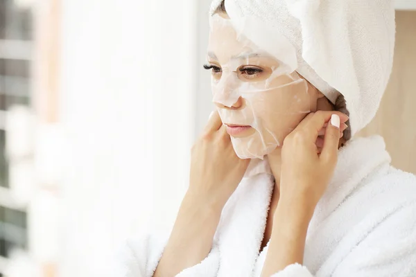 Mulher bonita aplicando máscara de folha de papel em seu rosto branco — Fotografia de Stock