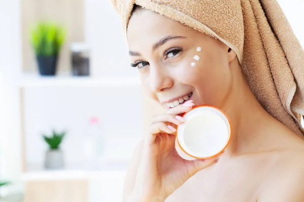 Hermosa mujer que aplica crema hidratante en su cara. — Foto de Stock