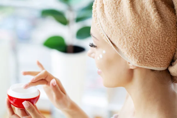 Hermosa mujer que aplica crema hidratante en su cara. — Foto de Stock