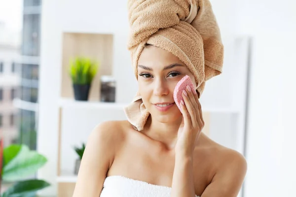 Jovem mulher feliz em toalha fazendo massagem facial com esfoliação facial orgânica no banheiro elegante. — Fotografia de Stock