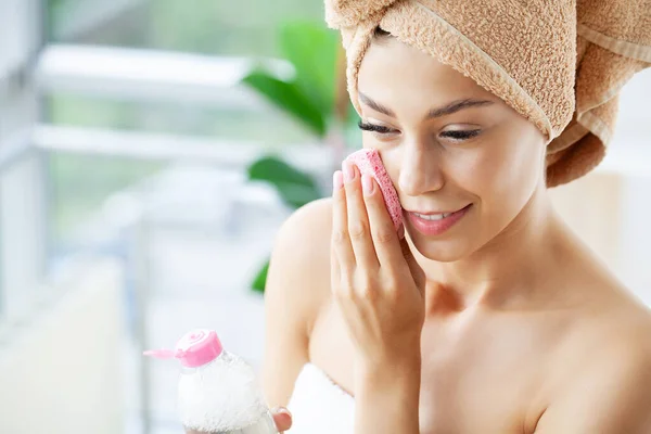 Giovane donna felice in asciugamano facendo massaggio facciale con scrub viso organico in bagno elegante. — Foto Stock