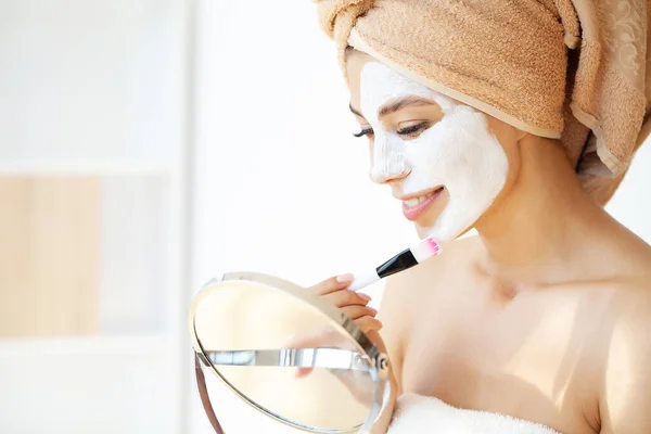 Jeune femme heureuse en serviette, application d'argile faciale Masque dans la salle de bain élégante. — Photo