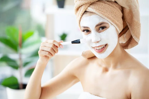 Jeune femme heureuse en serviette, application d'argile faciale Masque dans la salle de bain élégante. — Photo