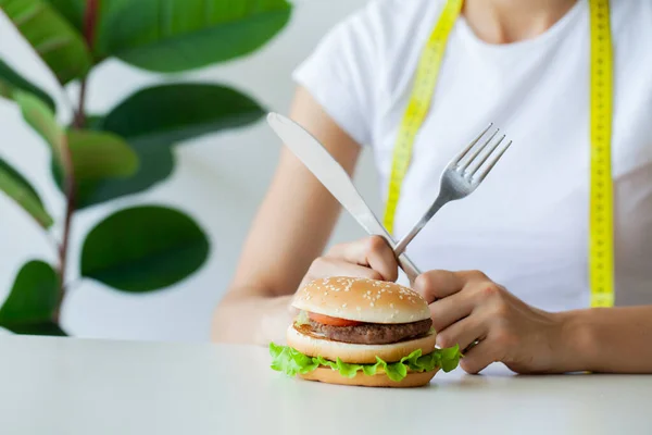 Ung kvinna som håller skadlig fett burgare med gul måttband — Stockfoto