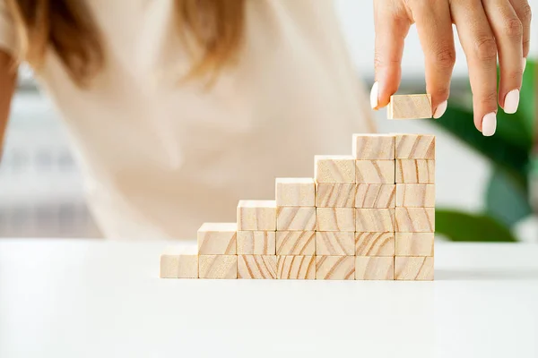 Woman hand stacking wooden blocks in shape of staircase.