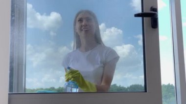 Sarı eldivenli ev hanımı, camları süngerle yıkıyor..