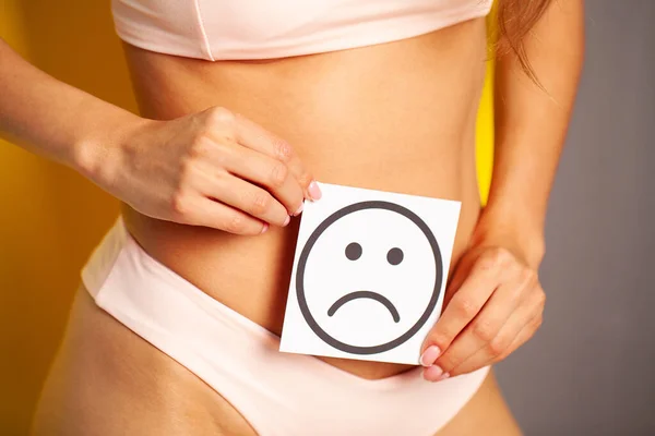 Mujer salud cuerpo femenino sosteniendo tarjeta blanca sonrisa triste cerca del estómago saludable — Foto de Stock