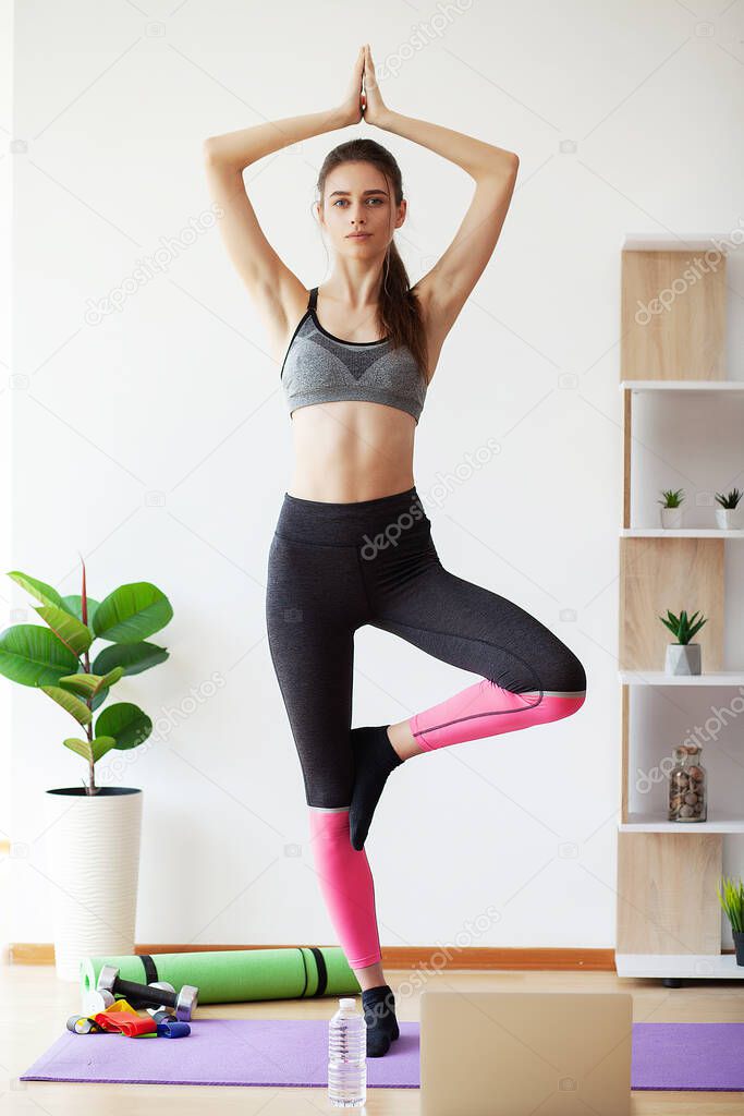 Attractive young woman doing yoga stretching yoga online at home