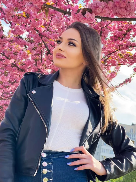 Belle jeune femme vêtue d'une veste noire se tient dans la couleur des fleurs de sakura au printemps. — Photo
