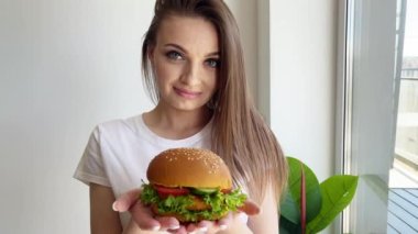 Sağlıksız yemek, kameraya sığır burger gösteren bir kadın..