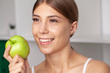 Sağlıklı beyaz dişli, yeşil elma tutan güzel bir kadın..