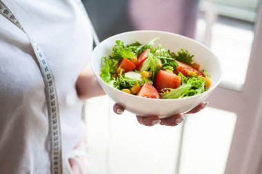 Bir kâse yeşil sağlıklı eko salata, elinde hafif mutfaktaki kadın.