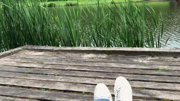 一个穿着白色运动鞋的男人的腿坐在湖边的码头上 — 图库视频影像