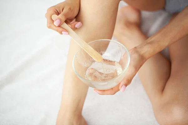 Beautician master holding bowl with hot wax for depilation epilation hair removal procedure.