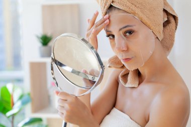 Avrupalı kadın yüzüne beyaz kumaş nemlendirici maske takıyor..