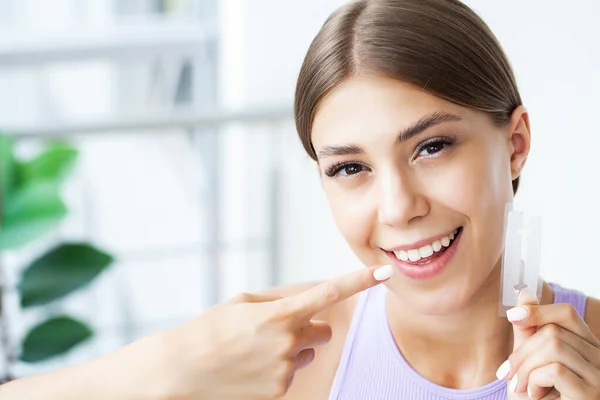 Teeth whitening, beautiful smiling woman holding a whitening strip