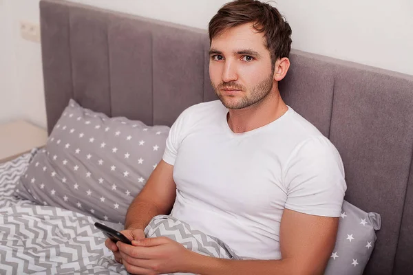 Młody Mężczyzna Siedzi Łóżku Używa Telefonu Komórkowego — Zdjęcie stockowe