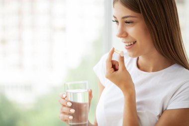 Gülümseyen kadın morina yağlı omega-3 ile hap alıyor ve sabahları bir bardak taze su tutuyor.