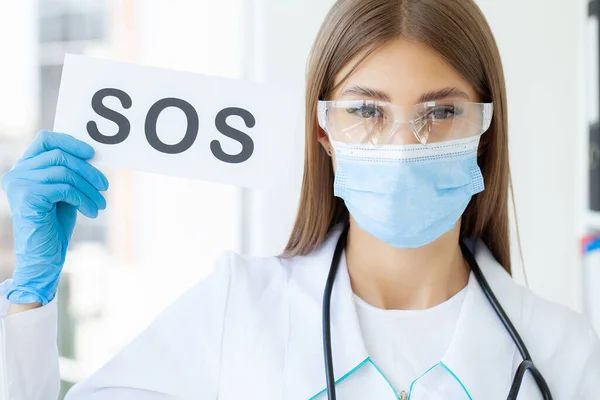 The doctor is holding a card with the Sos symbol in the office of the clinic.