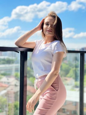 Panoramik pencerenin yanında kalan genç kadın modern evin terasında şehir manzaralı.