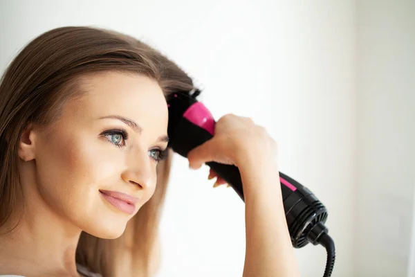 Woman straightening hair with straightener comb at home.